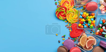 Foto de Varios caramelos coloridos, piruletas y macarrones. Dulces planos sobre fondo azul con espacio para copiar - Imagen libre de derechos