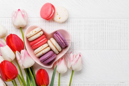 Photo for Pastel colorful tulips and vibrant macaroons fill a heart-shaped bowl, offering a delightful and charming scene perfect for celebrations or joyful moments - Royalty Free Image