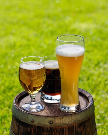 Variety of beer glasses on rustic wooden barrel. Sunny outdoor with copy space
