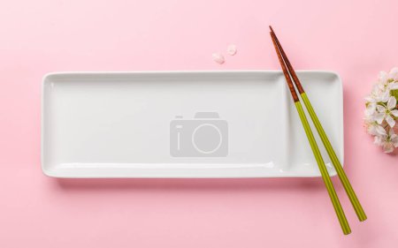 Photo for Empty plate on table adorned with cherry blossom branch and chopsticks, epitomizing Japanese food culture, providing ample copy space - Royalty Free Image