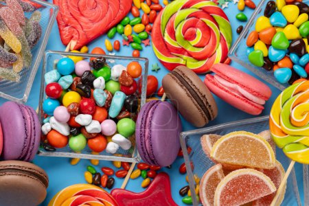 Téléchargez les photos : Divers bonbons colorés, sucettes et macarons. Poser des bonbons plats sur fond bleu - en image libre de droit