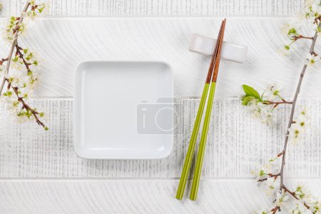 Téléchargez les photos : Assiette vide sur la table ornée d'une branche de cerisier et de baguettes, incarnant la culture alimentaire japonaise, offrant amplement d'espace pour copier - en image libre de droit