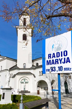 Photo for Krynica-Zdroj, Poland - October 17, 2022: Sign of Radio Maryja with Church of the Assumption of the Blessed Virgin Mary in Krynica-Zdroj town. Radio Marija is the most popular Catholic radio in Poland - Royalty Free Image