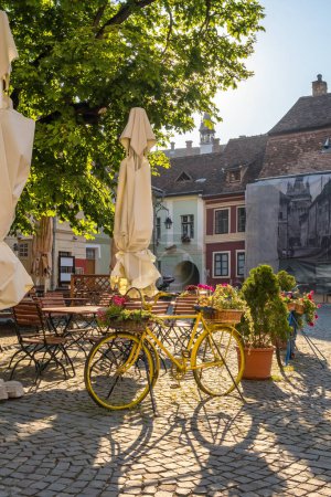 Photo for Street scene from the medieval city Sighisoara in Transilvania region of Romania. Cozy outdoor cafe at sunrise. Bicycle with flowers as a cafe decoration. - Royalty Free Image