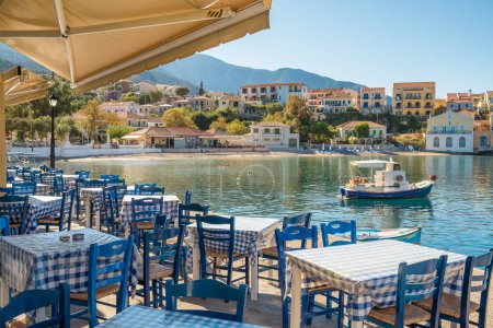 Photo for Idyllic view of the picturesque fishing village of Assos, Kefalonia island, Greece. Small fishing boat moored near traditional outdoor Greek restaurant in beautiful Assos village - Royalty Free Image