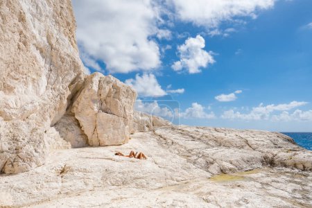 Unidentified couple sunbathe on the limestone rocky coast of Zakynthos island, Ionian Sea, Greece. Wild coast of Zante island. Greek holidays, summer vacation concept