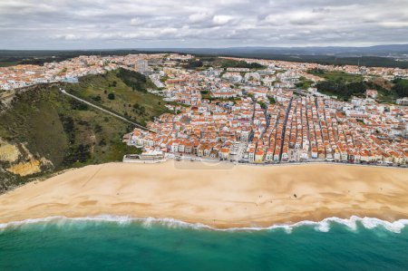Picturesque Portuguese coast town Nazare, Portugal. Historic buildings along long sand beach in Nazare town, seaside resort town, Portugal. Aerial drone view of the Nazare beach