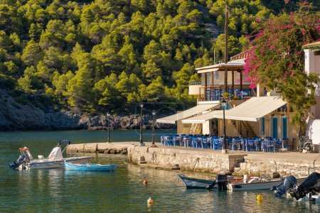 Photo for Idyllic view of the picturesque fishing village of Assos, Kefalonia island, Greece. Small fishing boat moored near traditional outdoor Greek restaurant in beautiful Assos village - Royalty Free Image