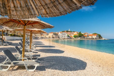 Une plage vide avec parasols et chaises longues vacantes sur la plage. Vue pittoresque sur la charmante ville de Primosten et la mer Adriatique en Croatie. Une destination de voyage parfaite pour les vacances d'été.