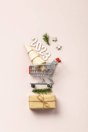 Photo for Holiday shopping 2023 concept. Miniature Christmas tree in shopping trolley cart on pink background - Royalty Free Image