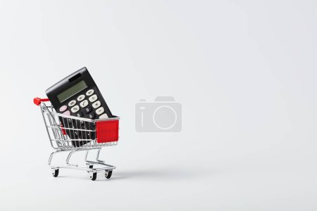 Photo for Shopping cart trolley and calculator on white background with copy space. Concept for grocery expenses and consumerism - Royalty Free Image