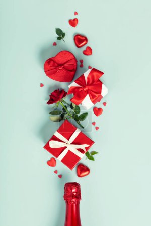 Téléchargez les photos : Champagne bottle with gift boxes, roses, chocolate and red hearts on blue background, top view, flat lay. Valentines day and party concept - en image libre de droit