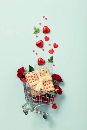 Foto de Shopping trolley with gift boxes, roses, chocolate and red hearts on blue background. Valentines Day. Wedding day. - Imagen libre de derechos
