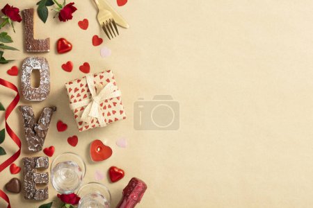 Photo for Valentines day composition with gift box in craft recycling paper, roses, candles, cutlery, champagne, chocolate and wooden letters, top view, flat lay, copy space - Royalty Free Image