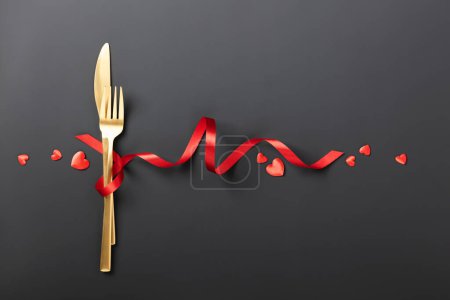 Foto de Fork and knife tied with a red ribbon on black background. Romantic dinner. Valentines Day. Top view, flat lay, copy space - Imagen libre de derechos