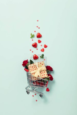 Téléchargez les photos : Shopping trolley with gift boxes, roses, chocolate and red hearts on blue background. Online stores. Winter Holiday Sales, Seasonal Sales, Black Friday, February 14 Valentines Day. Discounts and on - en image libre de droit