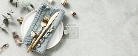 Téléchargez les photos : Banner. Table setting. A fashionable minimalistic plate with a linen napkin, Easter eggs and feathers on a gray background. Top view. Happy Easter holiday concept for cafes and restaurants. Copy space - en image libre de droit