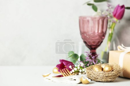 Foto de Easter table decorations with cutlery, spring flowers and golden eggs on light grey background copy space - Imagen libre de derechos