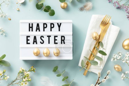 Téléchargez les photos : Easter table decorations. Stylish Easter brunch table setting with lightbox text Happy Easter, eggs, vintage cutlery, nests and spring branches on blue background top view flat lay - en image libre de droit