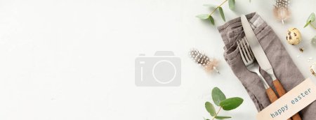 Easter table decorations. Stylish Easter brunch table setting with vintage cutlery, easter eggs and spring branches on light grey background top view flat lay copy space