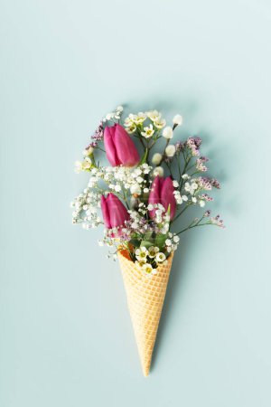 Foto de Ice cream cone with beautiful flowers on blue background flat lay top view. Summer minimal concept - Imagen libre de derechos