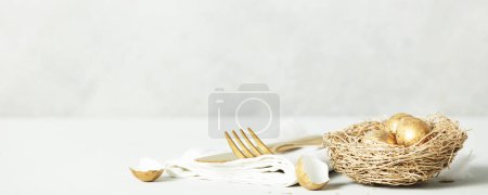 Easter table decorations with cutlery, spring flowers and golden eggs on light grey background copy space