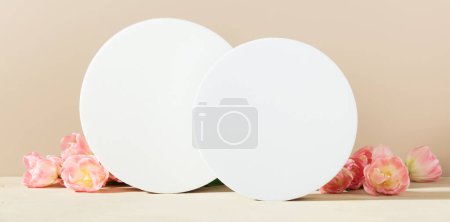 Foto de Pedestales en forma de círculo de espuma blanca y tulipanes de primavera en mesa beige con espacio para copiar, vista lateral. Fondo de maqueta de podio para productos. Plantilla publicitaria Plataforma de espuma. Pedestal geométrico abstracto. - Imagen libre de derechos