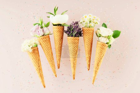 Foto de Colocación plana de conos de gofre con flores sobre fondo rosa claro pastel, vista superior. Concepto de humor primavera o verano - Imagen libre de derechos
