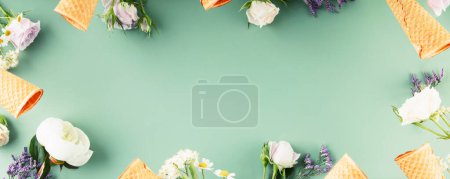 Photo for Flat-lay of waffle cones and flowers over pastel green background, top view, flat lay. Spring or summer mood concept, banner, copy space - Royalty Free Image