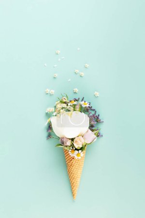 Téléchargez les photos : Nature morte créative de cône de gaufre avec des fleurs sur fond bleu clair pastel, vue de dessus. Concept minimal d'été - en image libre de droit