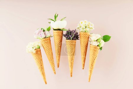 Foto de Colocación plana de conos de gofre con flores sobre fondo rosa claro pastel, vista superior. Concepto de humor primavera o verano - Imagen libre de derechos