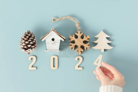Photo for Close up image of hand folds wooden numbers into the number of the new year 2024 on blue background - Royalty Free Image