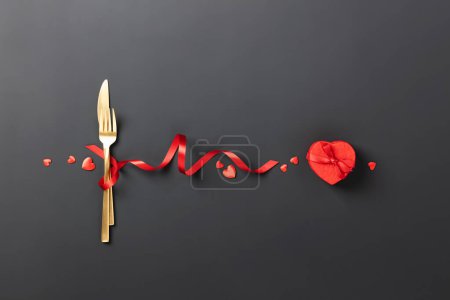 Téléchargez les photos : Fork and knife tied with a red ribbon on black background. Romantic dinner. Valentines Day. Top view, flat lay, copy space - en image libre de droit