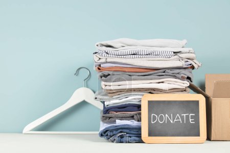 Photo for Chalkboard, Donation box and stack of clothes on table against blue background, copy space banner - Royalty Free Image