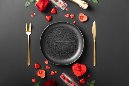 Téléchargez les photos : Beau cadre de table romantique avec assiette, fourchette, couteau, champagne et boîte cadeau sur fond sombre - en image libre de droit