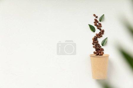 Téléchargez les photos : Grains de café en streaming sur une tasse en papier avec des ustensiles respectueux de l'environnement et feuilles vertes - en image libre de droit