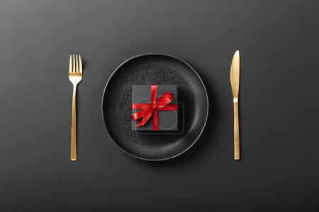 Téléchargez les photos : Beautiful romantic table setting with plate, fork, knife and gift box on dark background - en image libre de droit