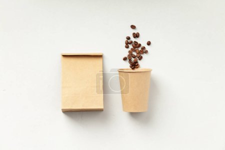 Foto de Una taza de café de papel junto a una bolsa marrón con granos de café sobre un fondo blanco. - Imagen libre de derechos