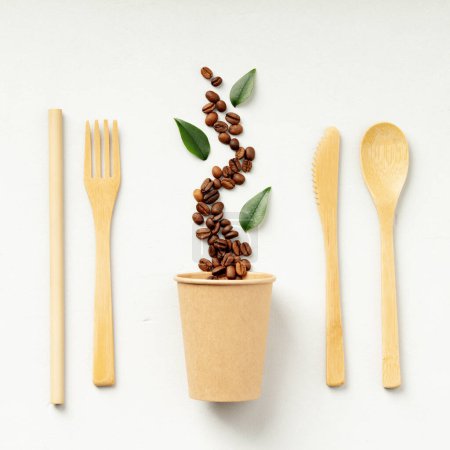 Foto de Granos de café que fluyen sobre una taza de papel con utensilios ecológicos y hojas verdes - Imagen libre de derechos