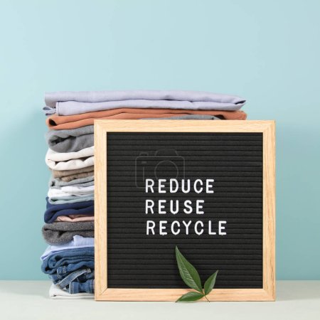 Schwarzer Briefkasten und Stapel gefalteter Kleidung auf blauem Hintergrund, reduzieren, wiederverwenden, recyceln Zitat. Null Verschwendung nachhaltigen Lebensstils. Kunststofffreies Konzept.