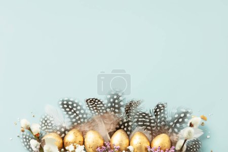 Téléchargez les photos : Cru d'œufs de caille dorée et de plumes de caille sur fond bleu. Belle composition minimaliste moderne de Pâques. Espace de copie, vue de dessus, plan plat - en image libre de droit