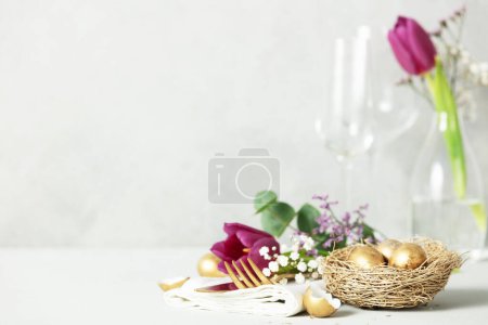 Foto de Decoraciones de mesa de Pascua con cubiertos, flores de primavera y huevos dorados en el espacio de copia de fondo gris claro - Imagen libre de derechos