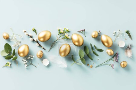 Foto de Composición pascual de huevos dorados de codorniz, plumas y flores de primavera sobre fondo azul pastel. Concepto de vacaciones de primavera. Fondo minimalista moderno de Pascua. Vista superior plano laico - Imagen libre de derechos