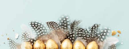 Téléchargez les photos : Cru d'œufs de caille dorée et de plumes de caille sur fond bleu. Belle composition minimaliste moderne de Pâques. Espace de copie, vue de dessus, plan plat - en image libre de droit