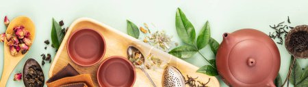 Photo for Overhead view of a wooden tray filled with assorted teas, cups, and a clay teapot, accentuated by fresh leaves against a calming pastel backdrop. - Royalty Free Image