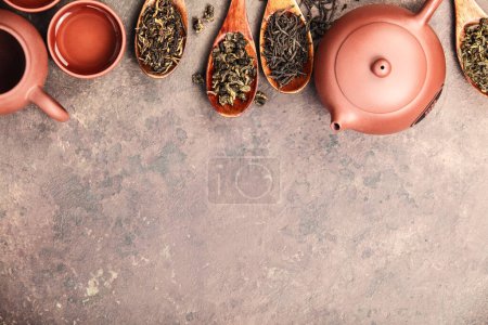 Photo for An assortment of loose tea leaves displayed on wooden spoons, with a traditional ceramic teapot and cups on a stone background - Royalty Free Image