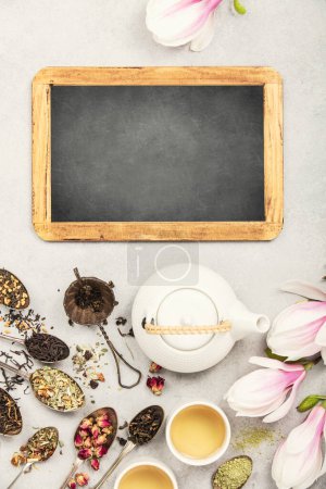 A tea lovers dream with a variety of loose-leaf blends, teapot, cups, and a blank chalkboard, all laid out on a textured surface, waiting for tasting notes or a personal message