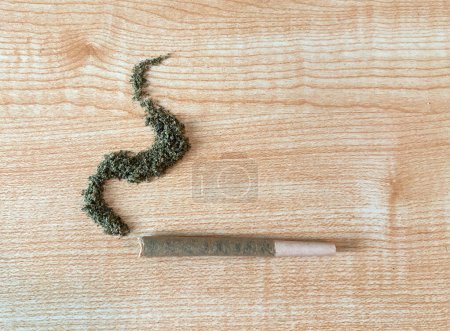 Rolled marijuanna flower joint on top of a wooden table, pre roll. Loose bud in the shape of smoke. 