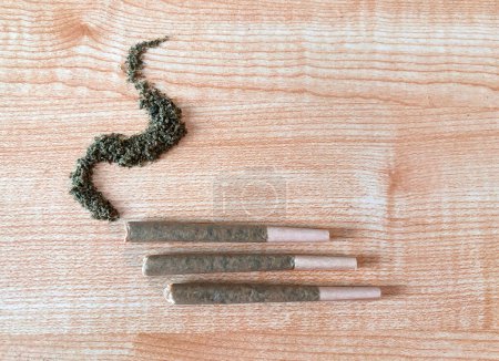 Ein paar Gramm gerollte Marihuana-Blüten auf einem Holztisch, vorgerollt, lose Knospe in Form von Rauch