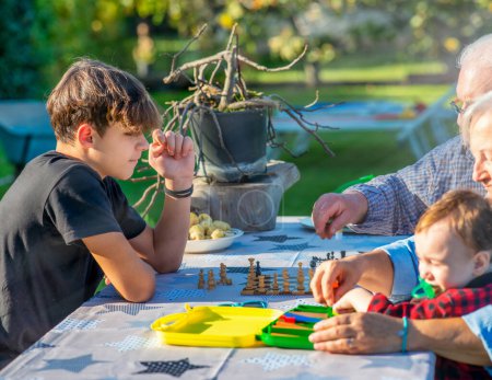 Foto de Abuelos y nietos jugando juntos al aire libre en una tarde soleada en los juegos de mesa - Imagen libre de derechos